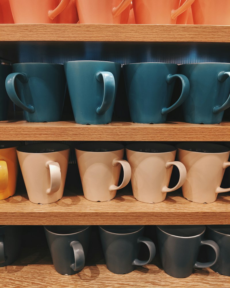 Blue ceramic mugs lined up on a wooden shelf