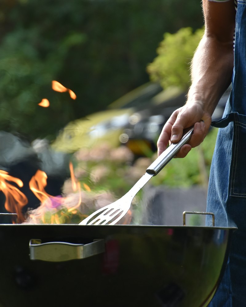 Someone turning food on a fire-lit backyard grill